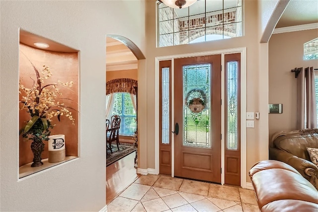 foyer entrance with light tile patterned floors, baseboards, arched walkways, and ornamental molding