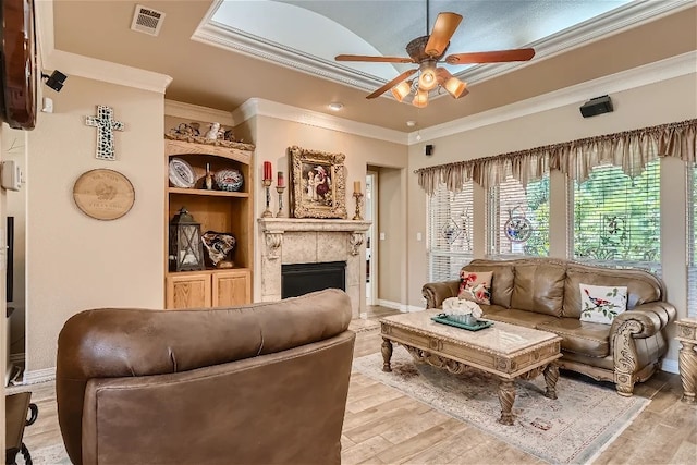 living room featuring a tray ceiling, visible vents, light wood finished floors, and a tile fireplace