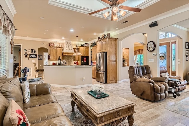 living room featuring visible vents, ornamental molding, light wood-style flooring, arched walkways, and a ceiling fan