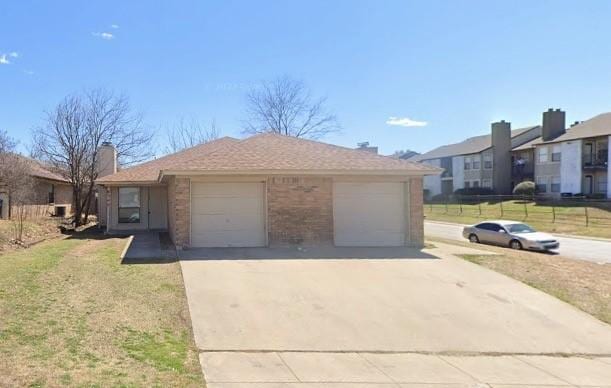 single story home with brick siding, an attached garage, a front lawn, a chimney, and driveway