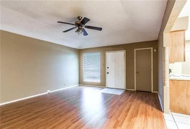 spare room featuring a textured ceiling, a ceiling fan, light wood-type flooring, and baseboards