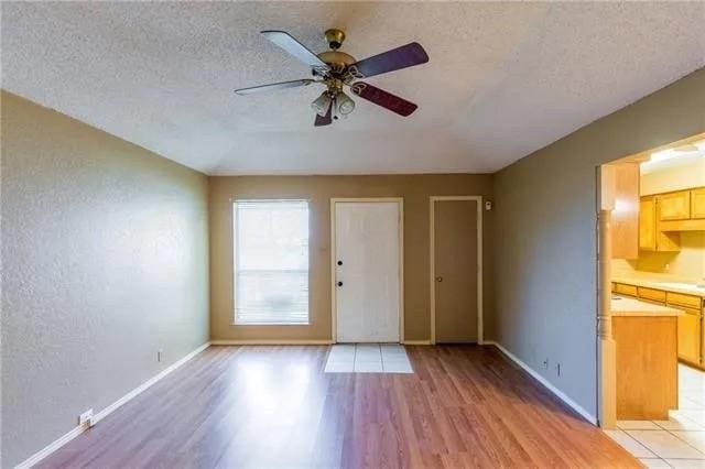 interior space with a ceiling fan, baseboards, a textured ceiling, a textured wall, and light wood-type flooring