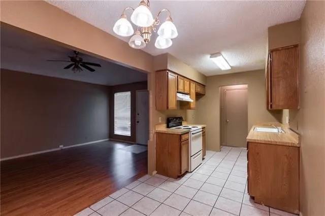 6743 Westcreek Dr, Fort Worth, TX 76133 - kitchen featuring brown cabinetry, white electric stove, a sink, light countertops, and ceiling fan with notable chandelier