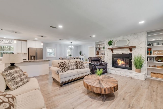 living room featuring a stone fireplace, built in features, light wood-style floors, and visible vents