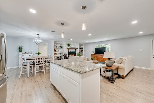 kitchen with a kitchen island, a stone fireplace, light wood-style flooring, and white cabinets