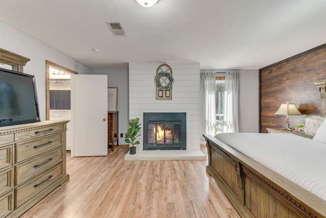 bedroom featuring visible vents, a large fireplace, light wood-style flooring, and ensuite bathroom