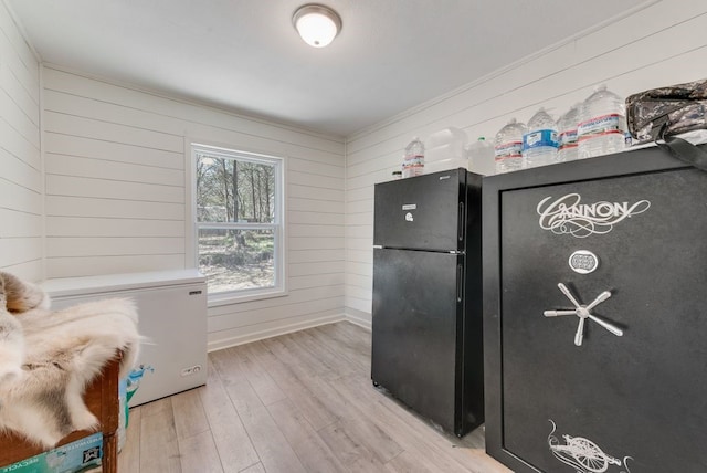 kitchen featuring baseboards, light wood finished floors, freestanding refrigerator, wood walls, and fridge