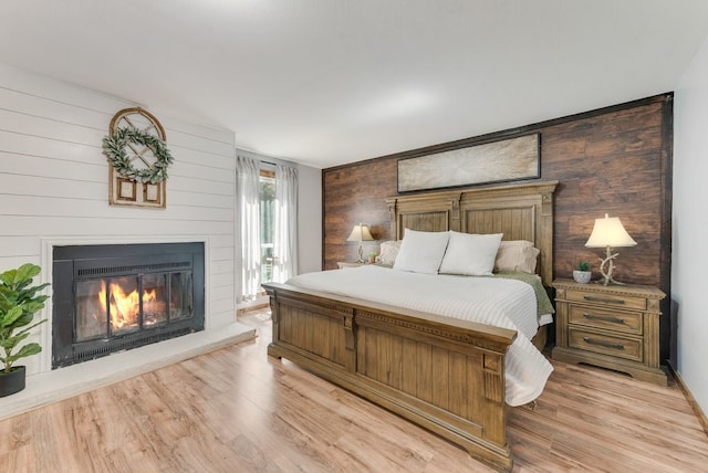 bedroom featuring a glass covered fireplace and light wood-style floors