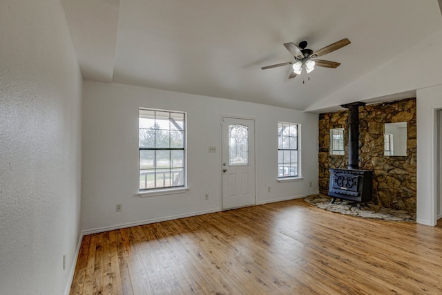 entryway with a wealth of natural light, vaulted ceiling, a wood stove, and hardwood / wood-style flooring