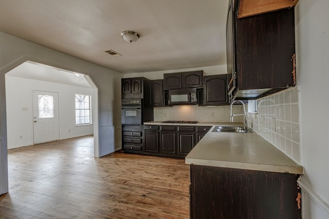 kitchen featuring light wood finished floors, arched walkways, a sink, black appliances, and tasteful backsplash