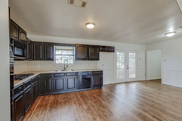 kitchen featuring visible vents, light wood finished floors, black appliances, a sink, and light countertops