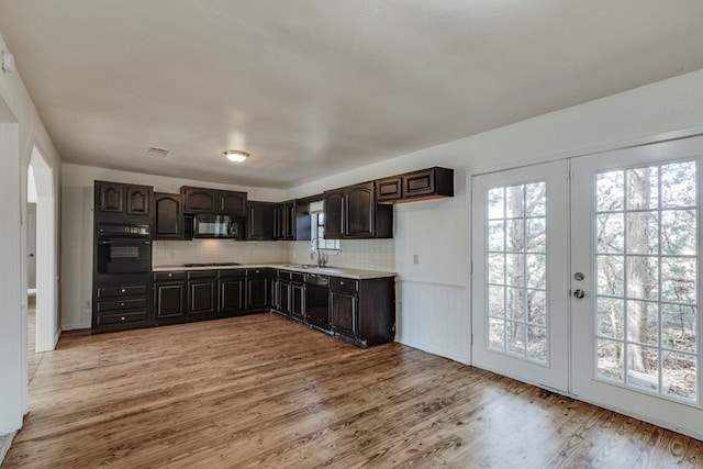 kitchen featuring light wood finished floors, light countertops, french doors, black appliances, and a sink