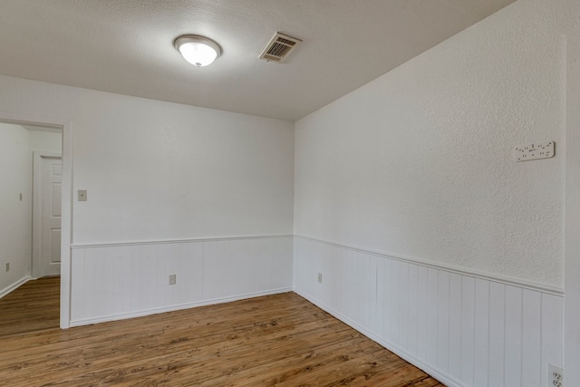 spare room featuring visible vents, a wainscoted wall, and wood finished floors