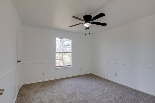 empty room with carpet flooring, a ceiling fan, and wainscoting