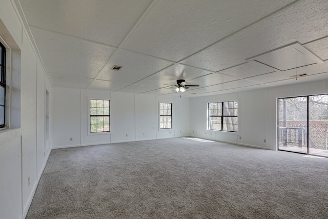 carpeted empty room featuring baseboards, visible vents, attic access, a drop ceiling, and ceiling fan