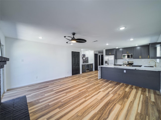 kitchen with light wood-style flooring, a sink, appliances with stainless steel finishes, a peninsula, and light countertops