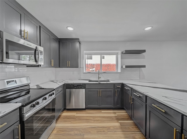 kitchen featuring light wood-style flooring, a sink, tasteful backsplash, appliances with stainless steel finishes, and light stone countertops