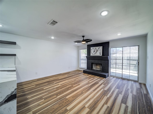 unfurnished living room featuring visible vents, a brick fireplace, baseboards, ceiling fan, and wood finished floors