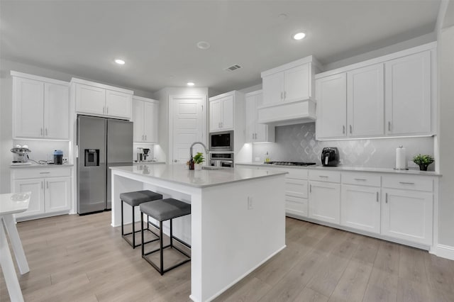 kitchen featuring light wood-type flooring, visible vents, a breakfast bar, stainless steel appliances, and white cabinets