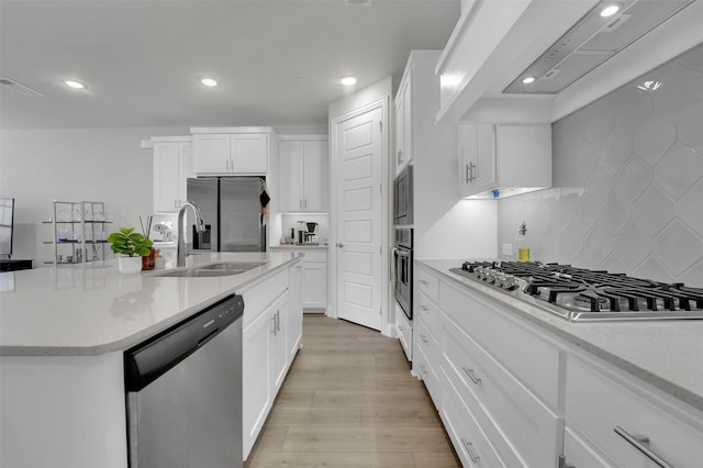 kitchen with light wood-style flooring, a sink, decorative backsplash, appliances with stainless steel finishes, and wall chimney exhaust hood