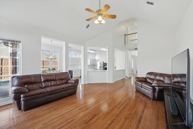 living room featuring light wood-style flooring, ceiling fan with notable chandelier, visible vents, and high vaulted ceiling