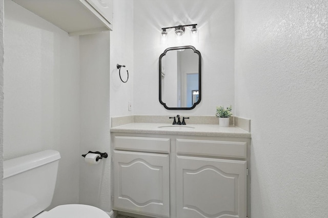 half bath with toilet, vanity, and a textured wall