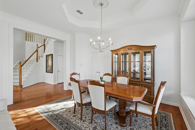 dining space with a tray ceiling, stairway, wood finished floors, and visible vents