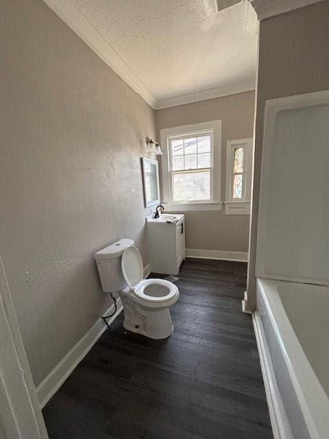 bathroom featuring toilet, ornamental molding, a textured ceiling, wood finished floors, and baseboards