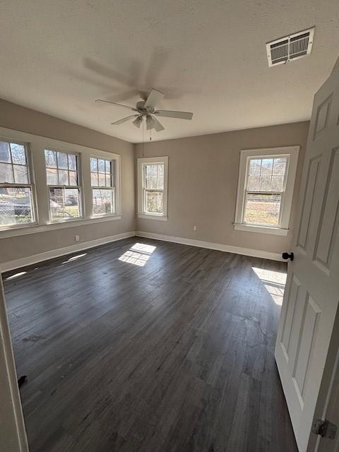 spare room featuring dark wood finished floors, visible vents, a ceiling fan, and baseboards