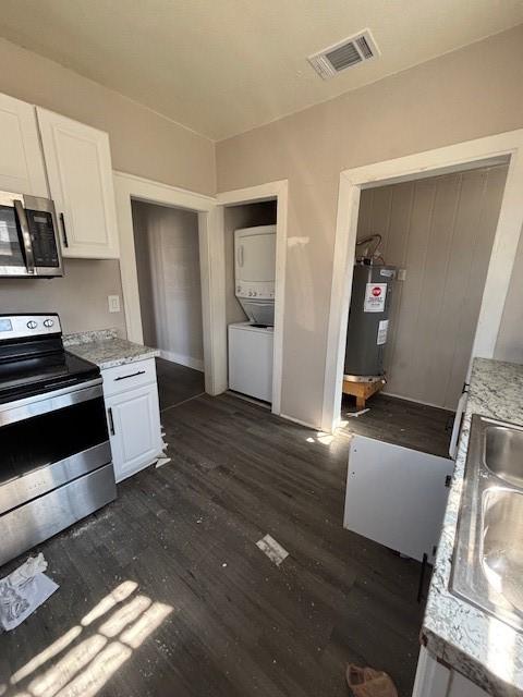 kitchen featuring visible vents, water heater, stainless steel appliances, stacked washer and dryer, and white cabinets