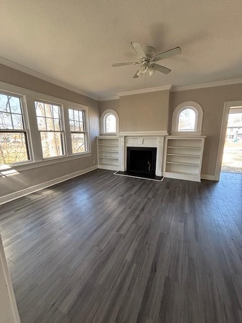 unfurnished living room with dark wood-style floors, baseboards, a fireplace with raised hearth, and ornamental molding