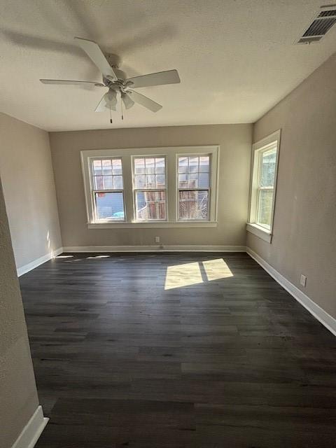 empty room with dark wood-style flooring, visible vents, and a wealth of natural light