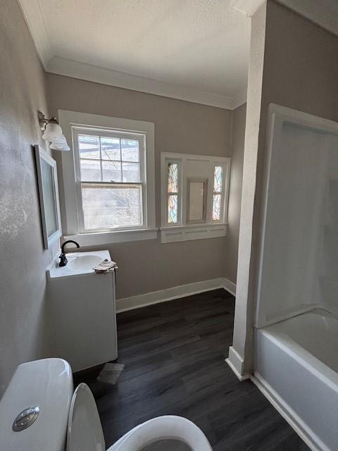 bathroom with toilet, ornamental molding, wood finished floors, baseboards, and vanity