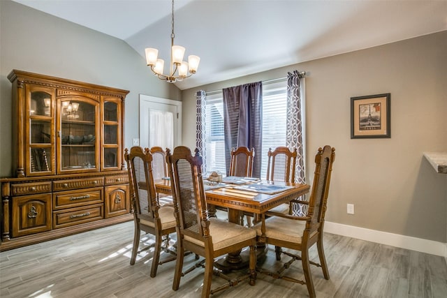 dining space featuring baseboards, lofted ceiling, a notable chandelier, and light wood finished floors