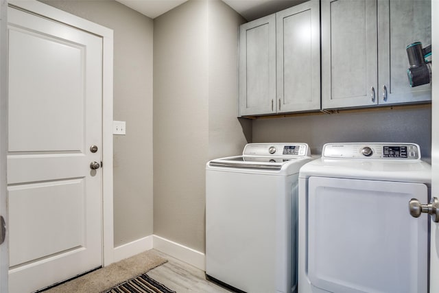 laundry area with light wood-type flooring, baseboards, cabinet space, and separate washer and dryer