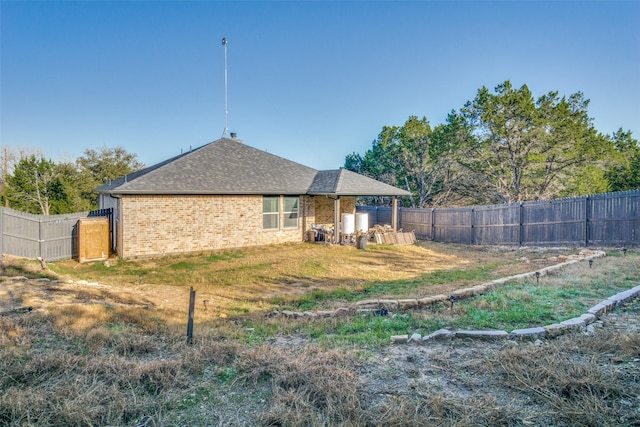 back of property with brick siding, a fenced backyard, and roof with shingles