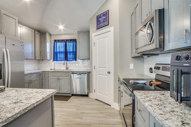 kitchen with a sink, stainless steel appliances, light wood-style floors, decorative backsplash, and light stone countertops