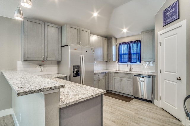 kitchen with a sink, light stone counters, appliances with stainless steel finishes, a peninsula, and light wood finished floors