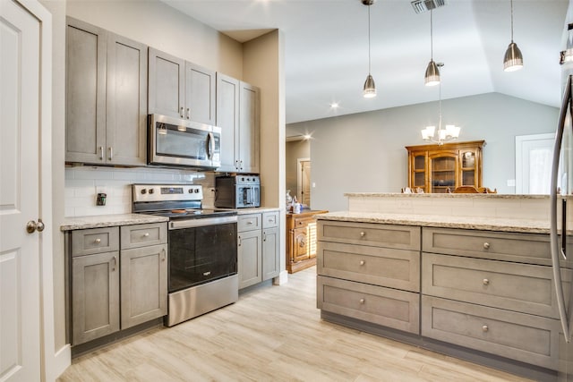 kitchen with lofted ceiling, light wood-style floors, appliances with stainless steel finishes, a notable chandelier, and tasteful backsplash