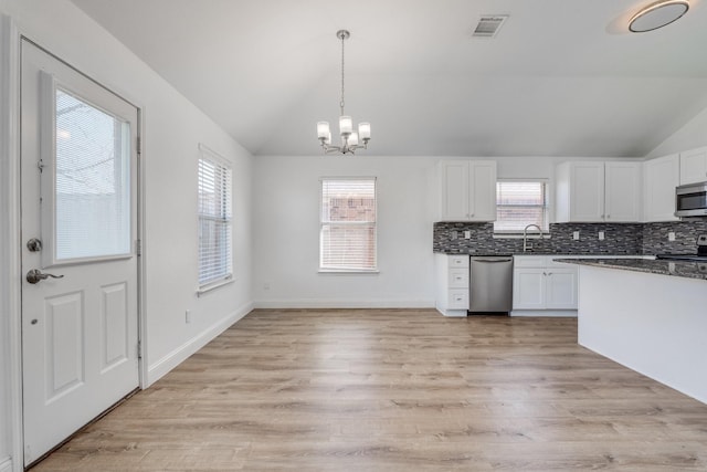 kitchen with dark countertops, visible vents, vaulted ceiling, stainless steel appliances, and white cabinetry