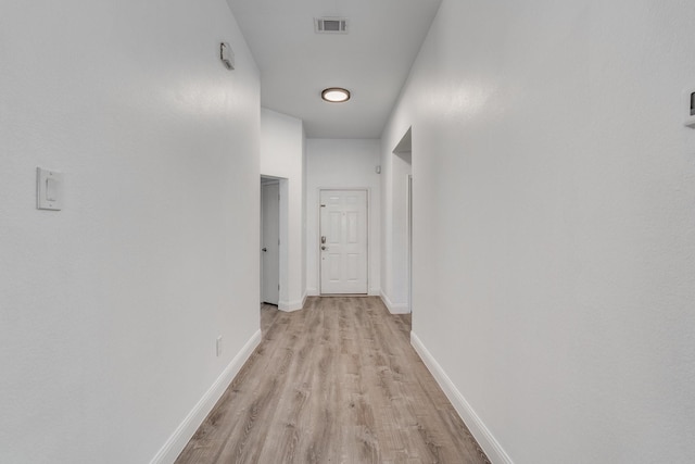 corridor with light wood-style floors, visible vents, and baseboards