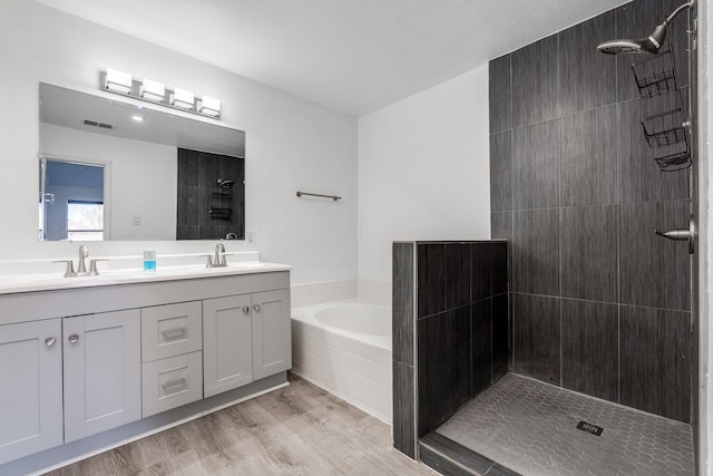 bathroom with a tile shower, double vanity, wood finished floors, and a sink