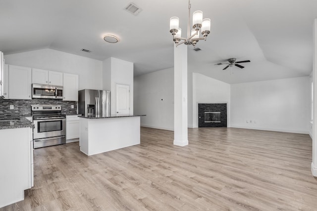 kitchen featuring a kitchen island, tasteful backsplash, stainless steel appliances, a stone fireplace, and lofted ceiling