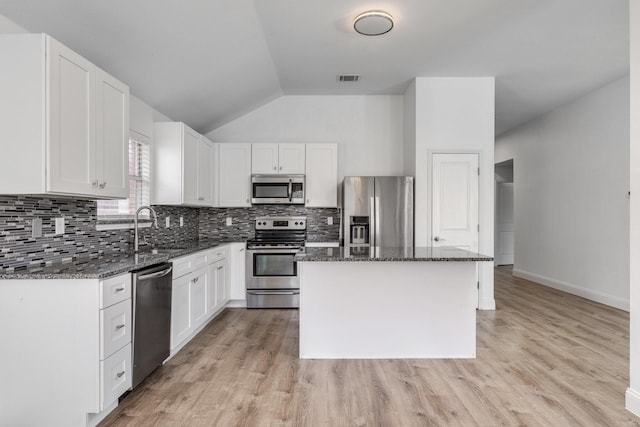 kitchen featuring dark stone countertops, appliances with stainless steel finishes, a center island, and a sink