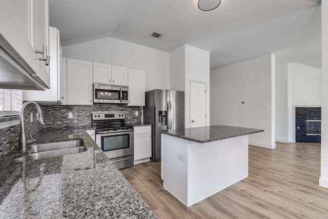 kitchen featuring a sink, stainless steel appliances, white cabinets, a glass covered fireplace, and a center island