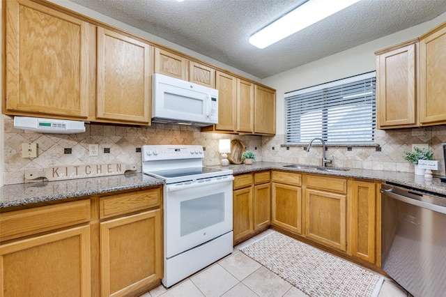 kitchen with white appliances, light tile patterned floors, stone countertops, a sink, and decorative backsplash