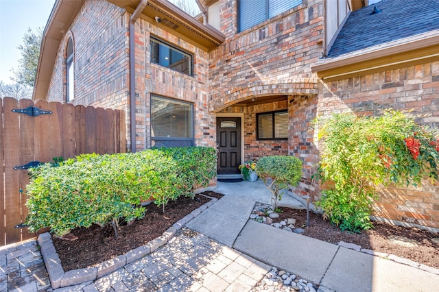 doorway to property with brick siding, roof with shingles, and fence