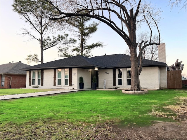 ranch-style home with fence, a front yard, a shingled roof, brick siding, and a chimney