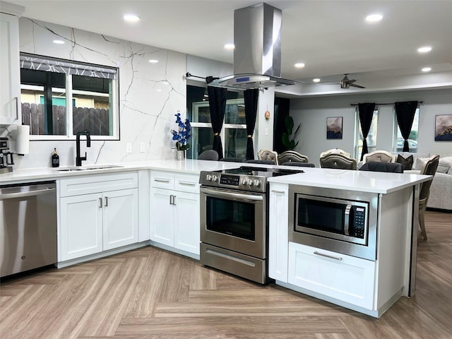 kitchen featuring a sink, island exhaust hood, recessed lighting, appliances with stainless steel finishes, and a peninsula