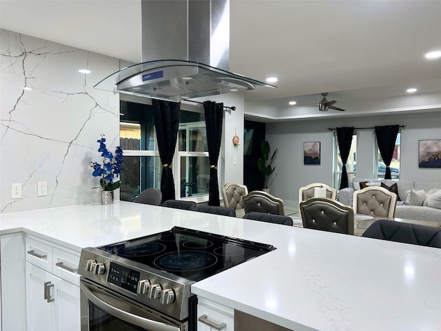 kitchen featuring open floor plan, recessed lighting, island exhaust hood, electric stove, and white cabinetry